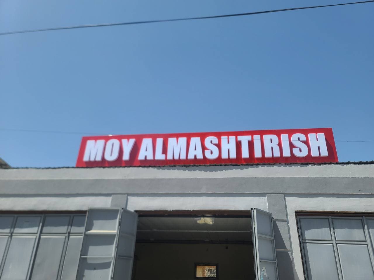 Bino tomiga oʻrnatilgan qizil fonli oq harfli peshlavha